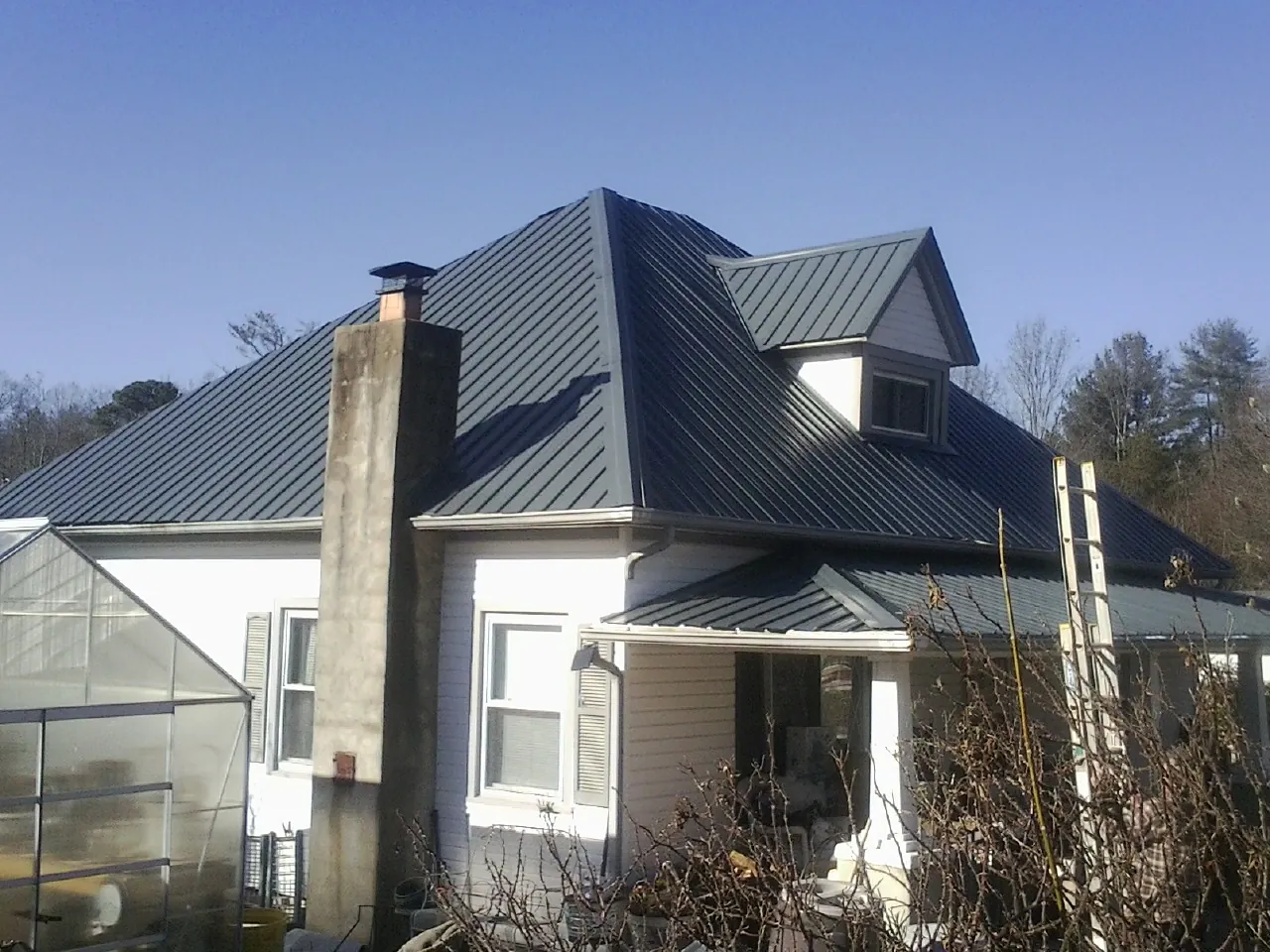 Dark blue standing seam metal roof on a white farmhouse with dormer in Quinby