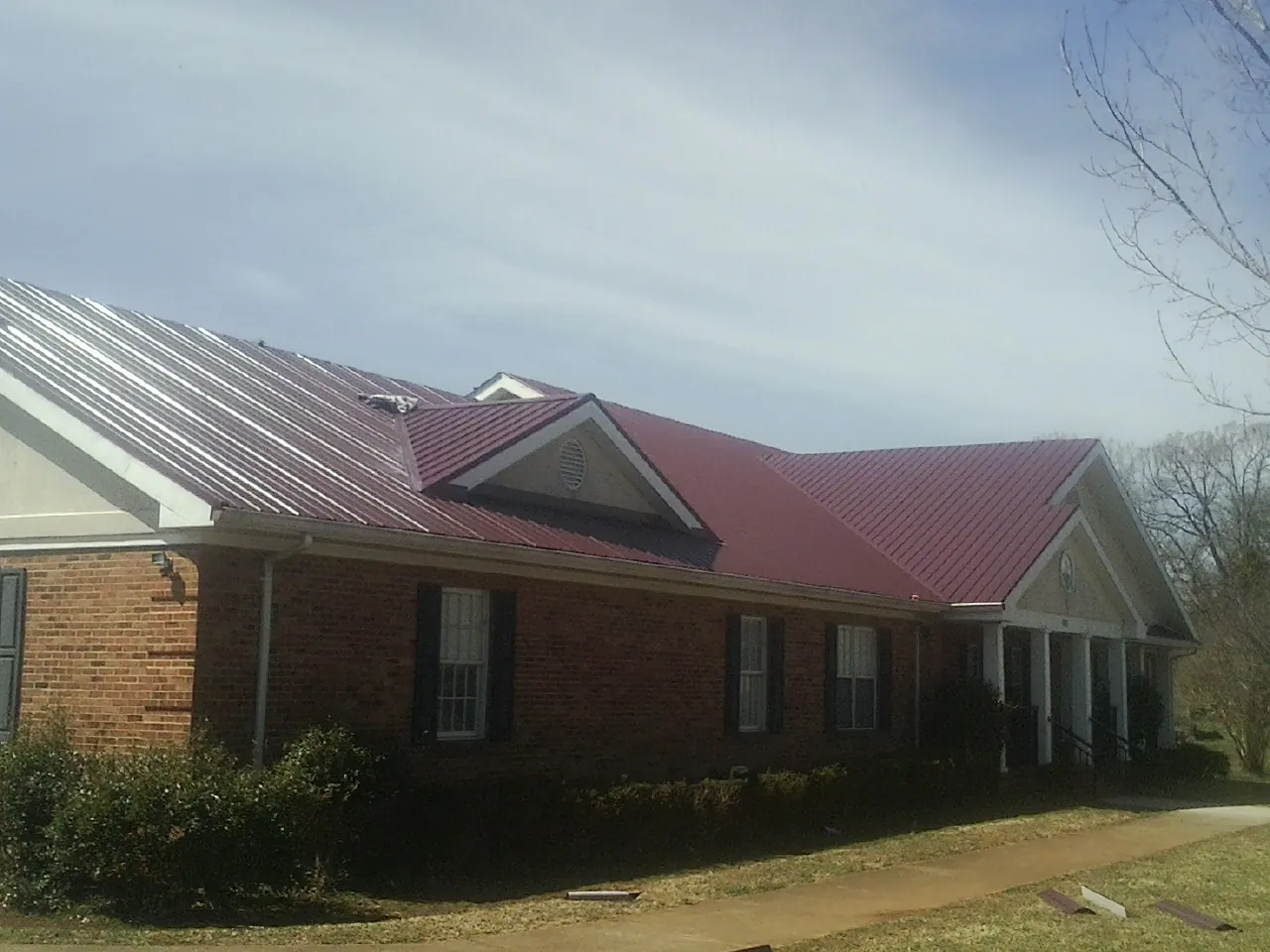 Red metal roof with gabled entries on a long brick building, from a Hail Damage Roof Repair job in Quinby