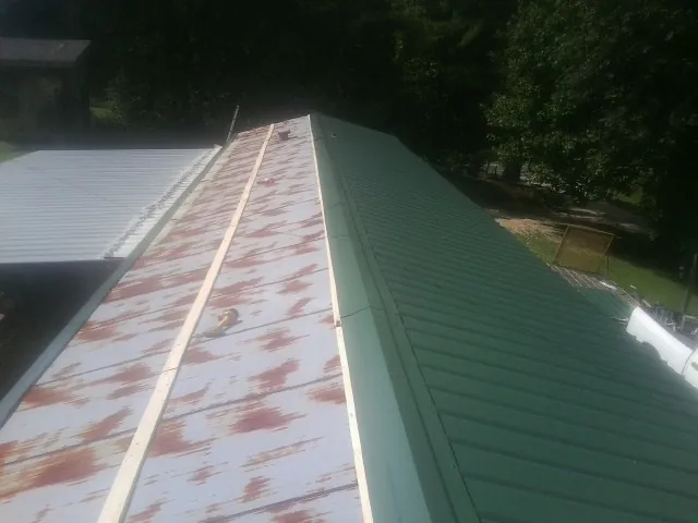 Old rusted panels beside newly installed green metal roofing — Wind Damage Roof Repair by Roofing Brothers in Quinby