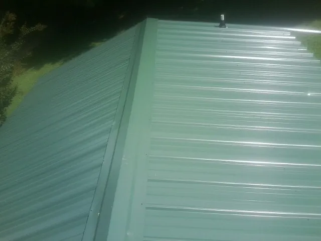 New green metal panels meeting at the ridge of a roof — Flat Roof Repair work by our crew in Quinby