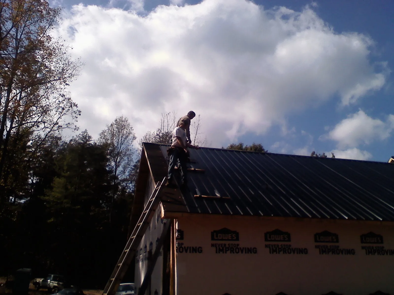 Roofer fastening dark metal panels high against a cloudy sky, from a Roof Inspection job in Quinby