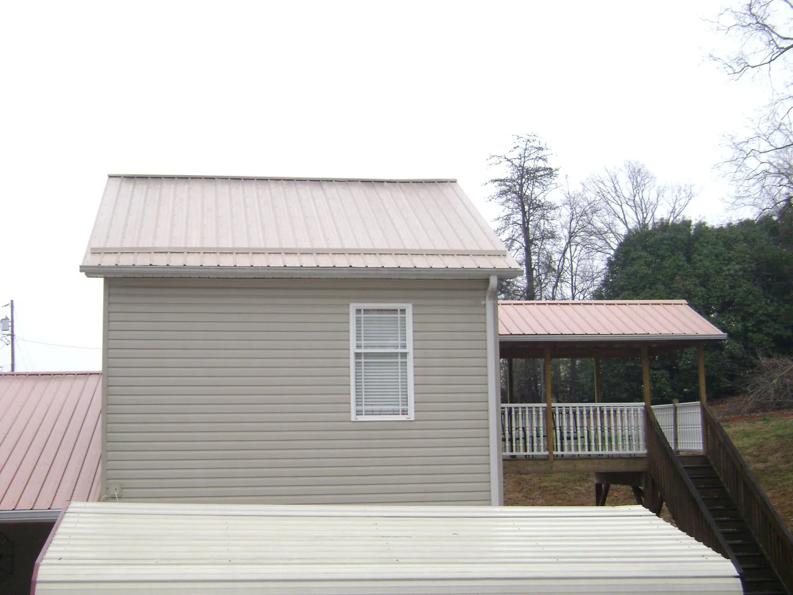 Tan metal roofs on a two story addition and attached porch, from a Roof Replacement job in Quinby